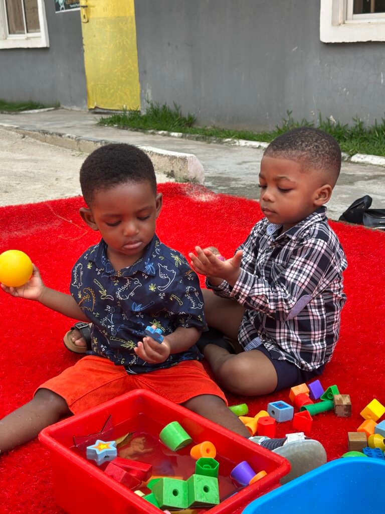 Toddlers playing with coloured building blocks on a red mat outdoors