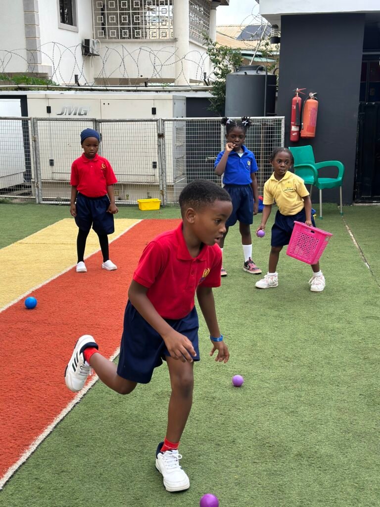 Children in coloured sports shirts racing to collect balls during a games lesson